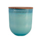 Vela grande en vaso de cristal de color  y tapa de madera con tres mechas.